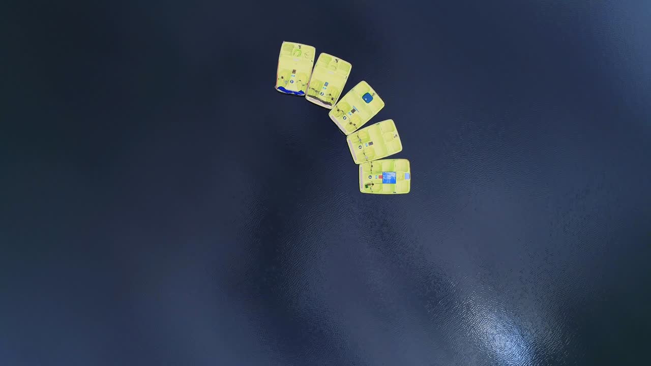 Looping aerial view of a few paddeleboats floating on lake in the scenic background. 4K.