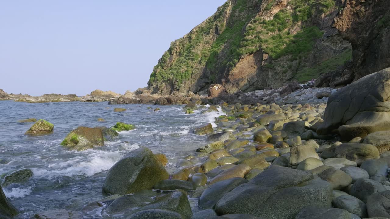 Pan across beautiful stone beach with cliffs and clear ocean