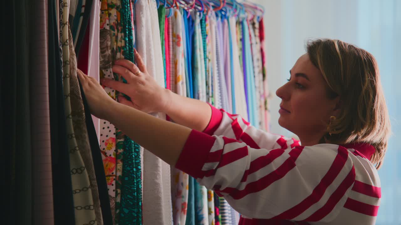 Woman touches fabric samples in bright, colorful textile store. She focuses closely, choosing material with care and interest. Scene captures calm, thoughtful shopping experience