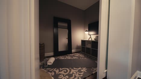 wide-push-in-shot-of-a-moody-dimly-lit-yoga-room-with-a-large-mirror,-lamp,-and-yoga-mat-on-the-floor