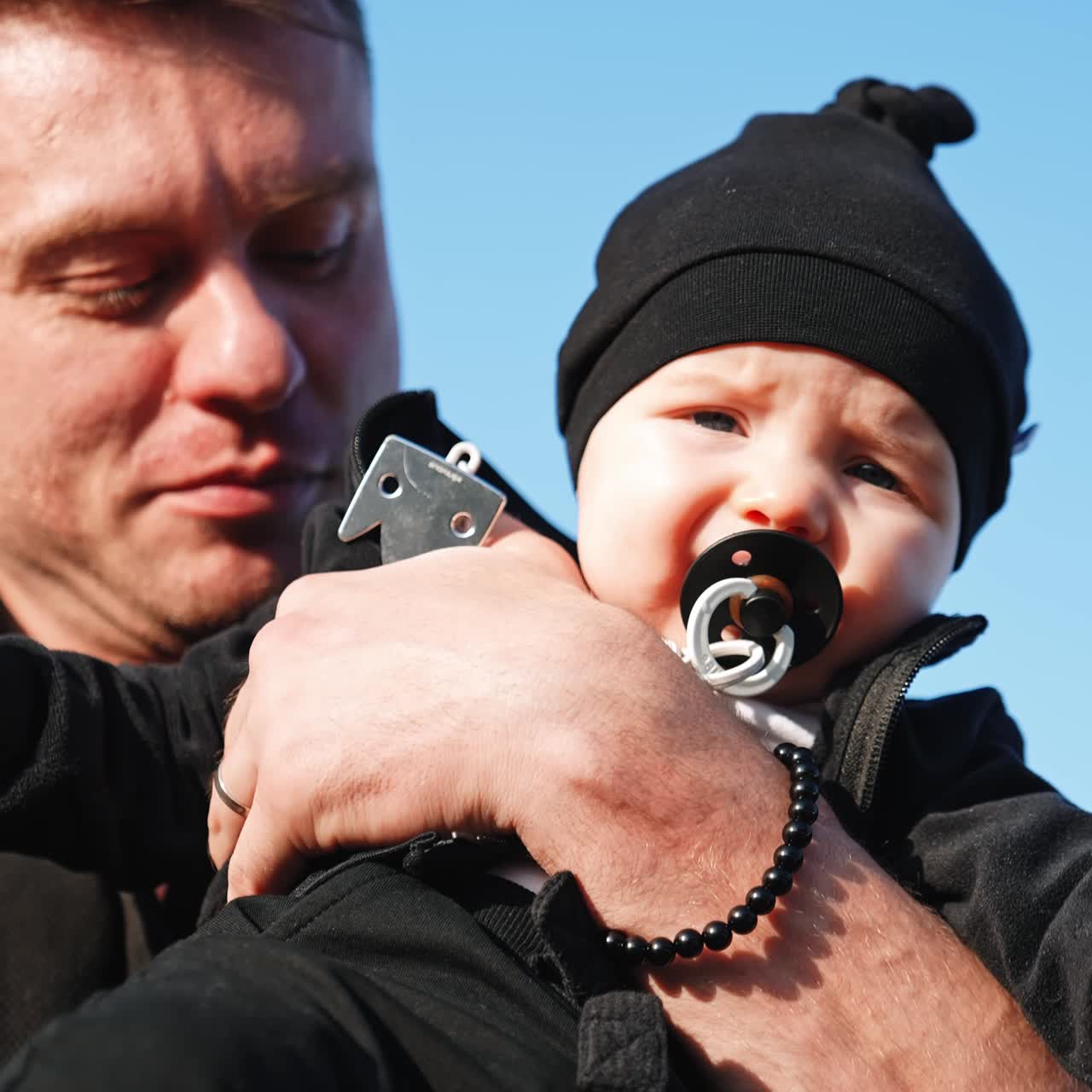 Kaukasisk mand med en lille dreng i armene. Sød baby med sut i munden, der rynker panden. Tæt på. Lodret skærm.