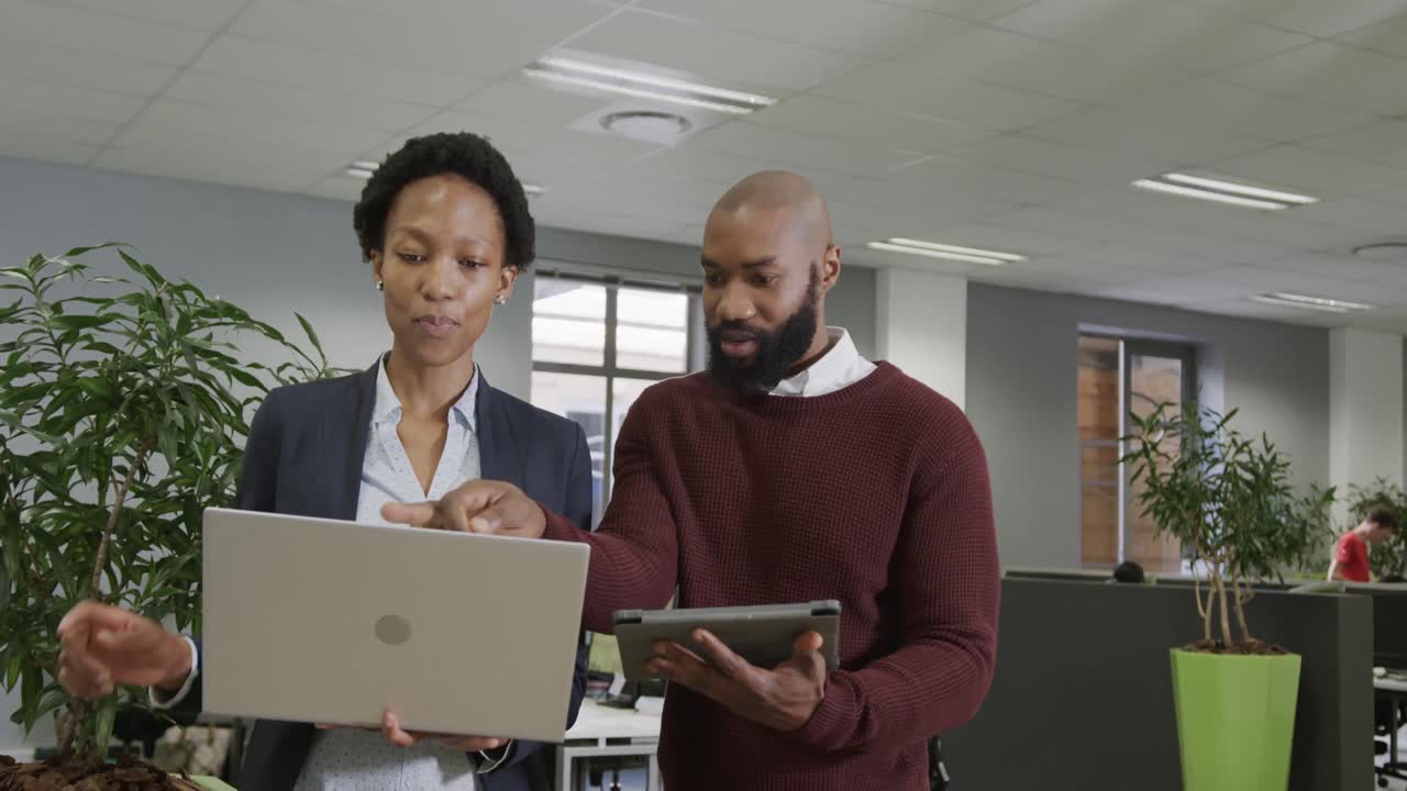 Professionisti afroamericani discutono di lavoro, utilizzando un laptop e un tablet in ufficio, al rallentatore.