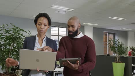 African-american-business-people-discussing-work,-using-laptop-and-tablet-in-office,-in-slow-motion