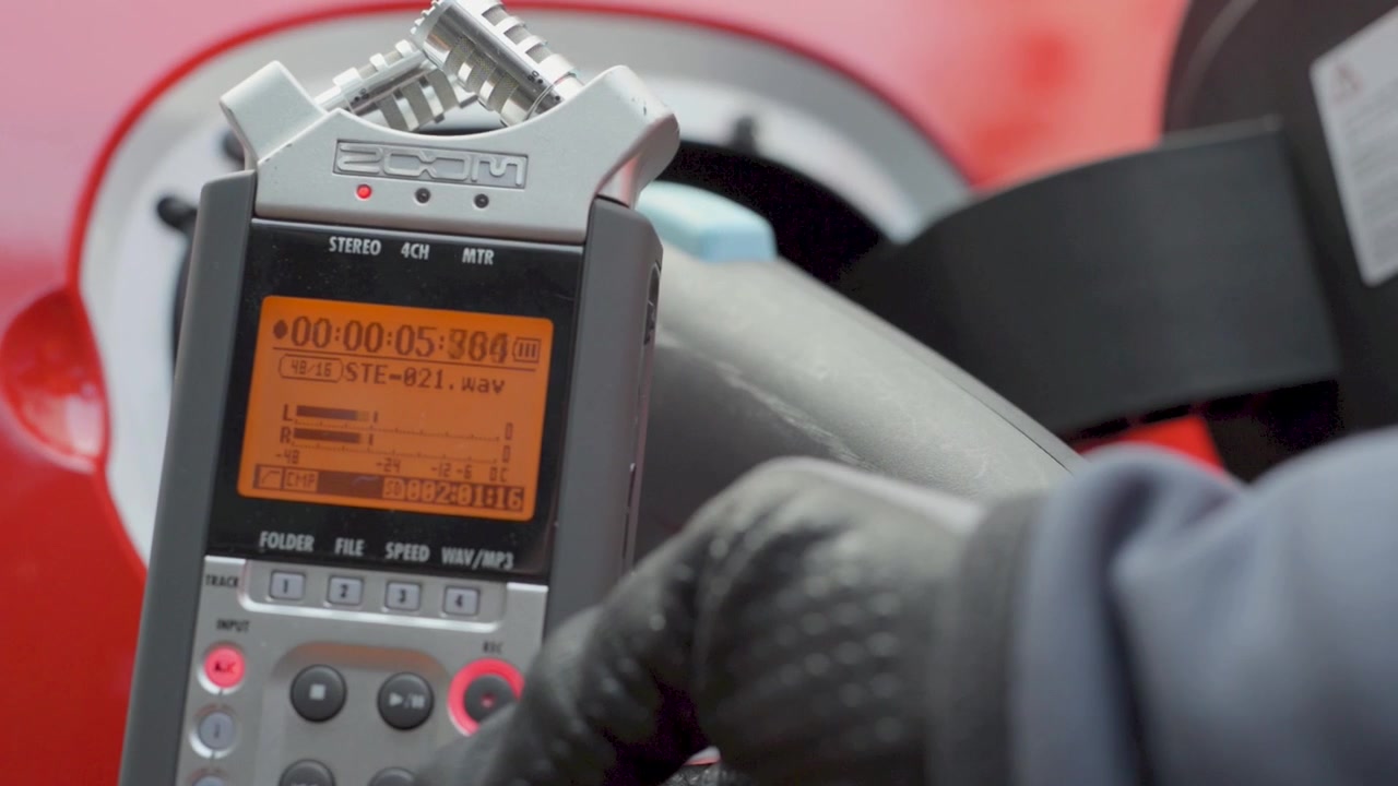 Gloved hand holds audio recorder near electric car charging port during charging