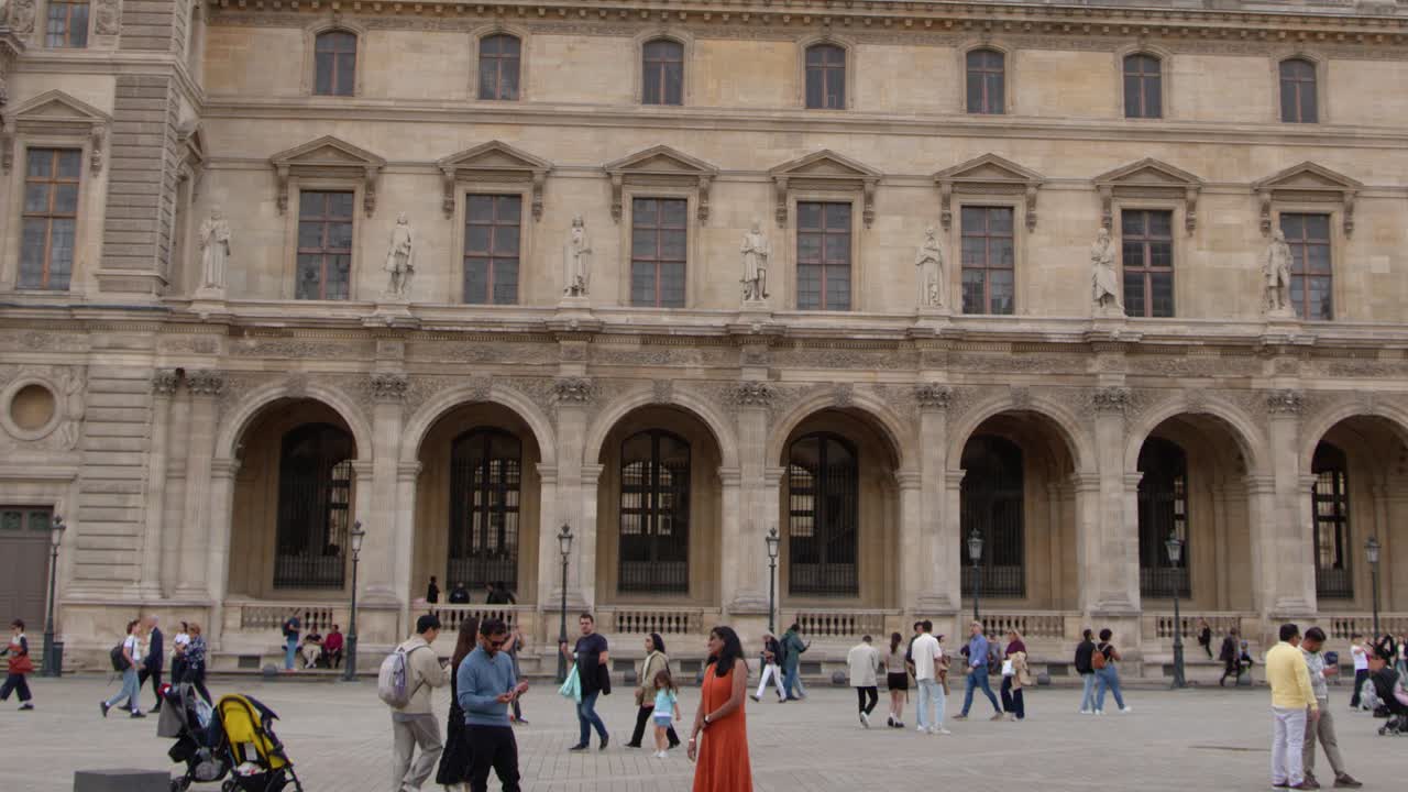 Un'ampia panoramica cattura turisti che esplorano il cortile storico in pietra di un museo parigino