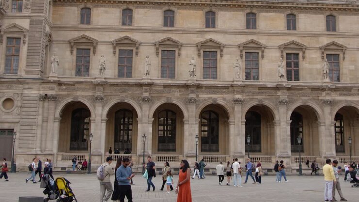 Un'ampia panoramica cattura turisti che esplorano il cortile storico in pietra di un museo parigino