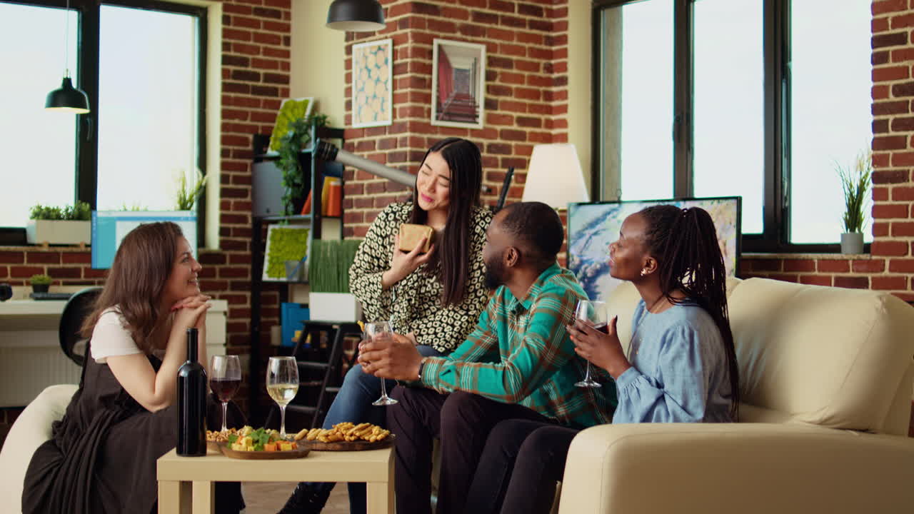 Cheerful group of people celebrating host anniversary, gifting neatly packaged present