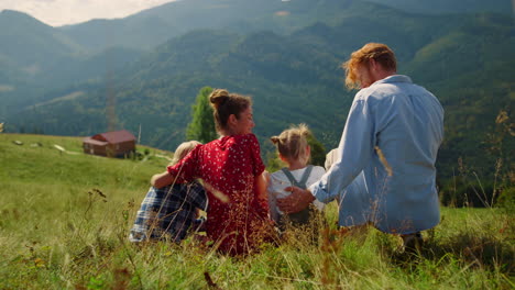 parents sitting grass mountains hill with children. family hugging on meadow.