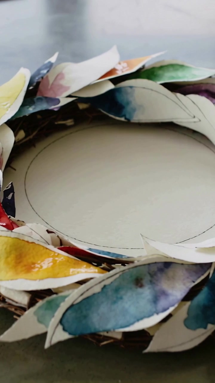 Vertical video: Panning camera across wreath on gray table as clip starts, revealing painted leaves