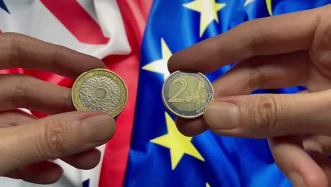 2 pound and 2 euro coins in hands on background of the uk and european union flags