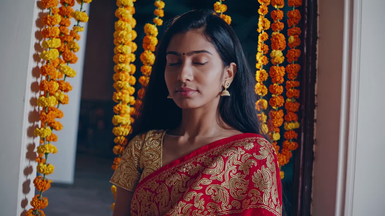 Woman in traditional attire stands gracefully in a doorway adorned with vibrant marigold flowers, embodying cultural elegance and serene beauty in a flowing sequence