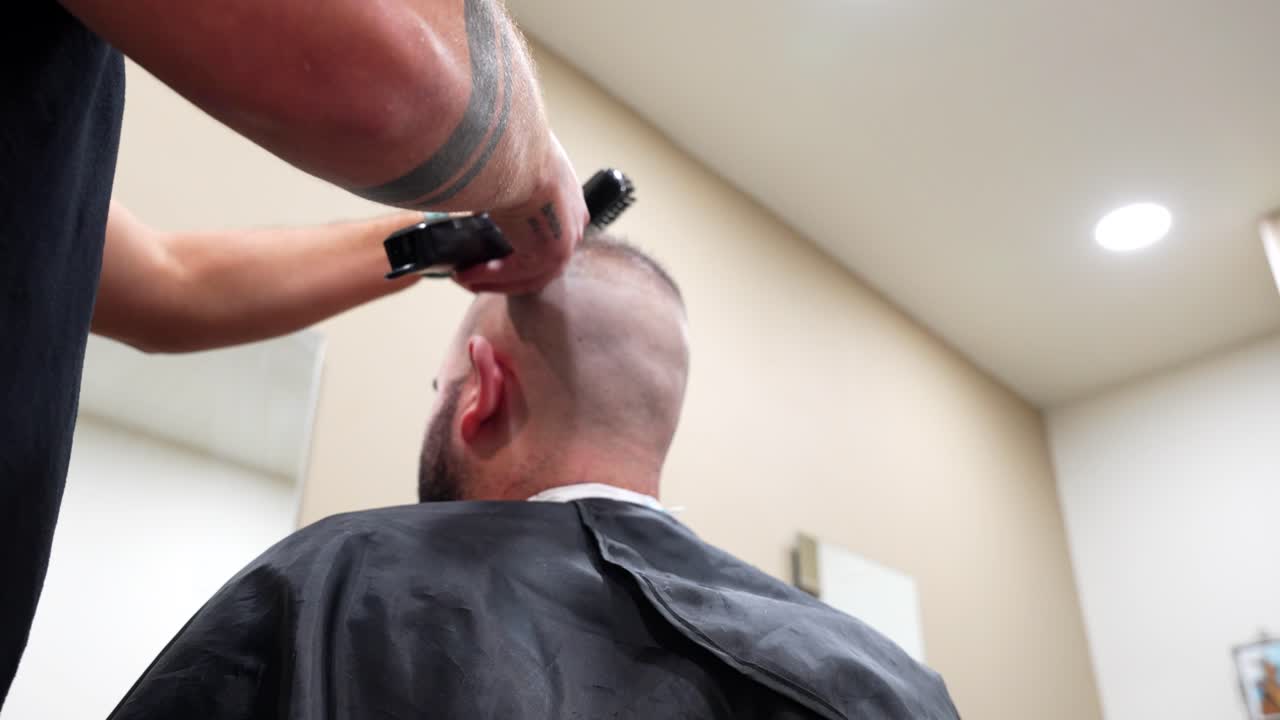 Tattooed barber arm cutting customer hair with a trimmer in modern barbershop environment
