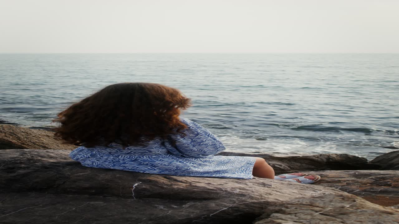 mujer sentada en las rocas junto al océano