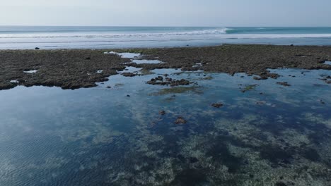 Low-angle-drone-shot-of-low-tide-reef-and-waves-in-Uluwatu-Bali-Indonesia