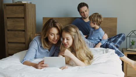 vista de cerca de una niña y su madre acostadas en la cama y viendo algo en la tableta