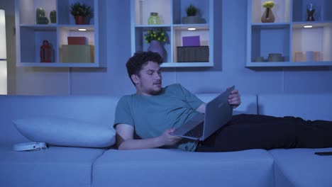 man watching horror movie on laptop at night. the man is frightened and tense.