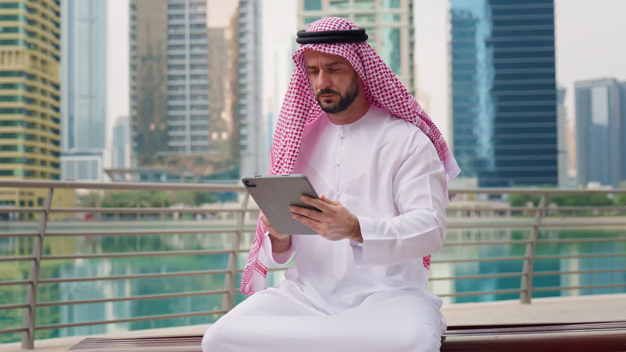 Uomo arabo mediorientale che indossa l'abito tradizionale kandura, utilizza un tablet digitale mentre è seduto in