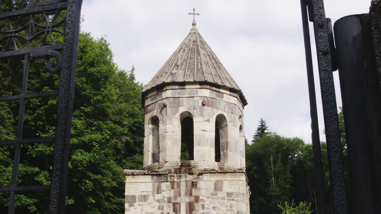 el campanario del monasterio mtsvane de piedra detrás de la puerta de barandilla de hierro abierta