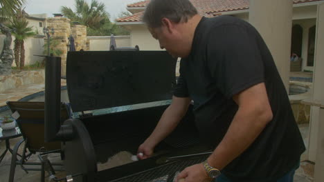 Man-scoops-ash-out-of-BBQ-pit-smoker-to-clean-it-before-cooking