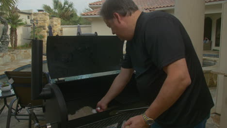 man scoops ash out of bbq pit smoker to clean it before cooking