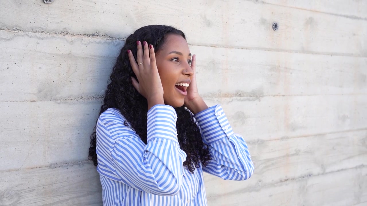 Portrait of a joyfully smiling woman with curly hair posing against a rough concrete wall