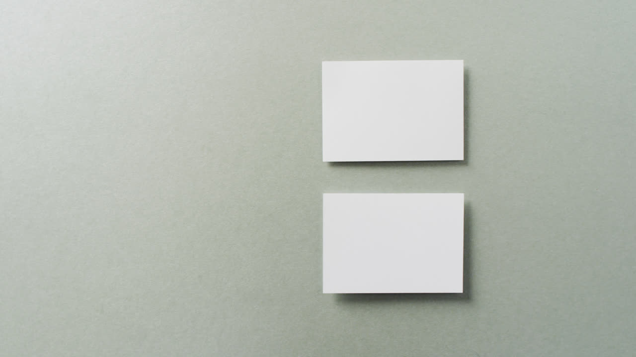 Overhead view of two white business cards arranged on grey background, copy space, slow motion