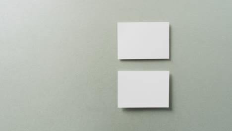 Overhead-view-of-two-white-business-cards-arranged-on-grey-background,-copy-space,-slow-motion