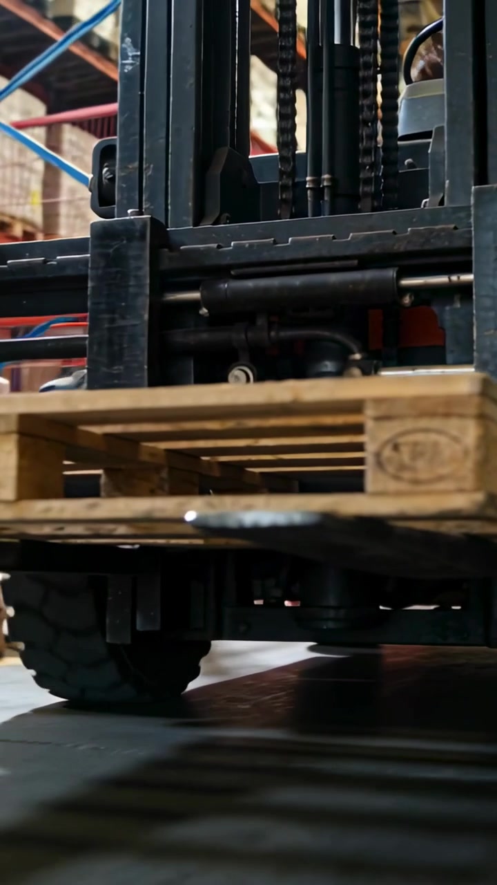 Video verticale: Carrello elevatore che si avvicina, solleva un pallet di legno vuoto in un magazzino, centrandolo per spostarlo.