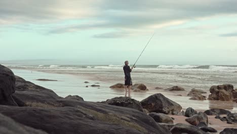 Pescador-Recreativo-Se-Encuentra-En-La-Arena-De-La-Playa-Mientras-Pesca-En-El-Surf