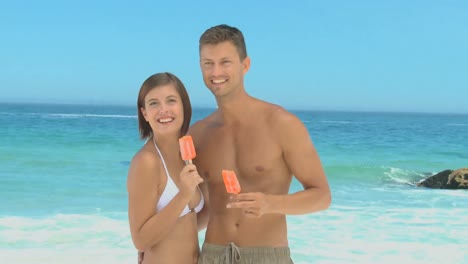 dulce pareja comiendo helados de agua en una playa