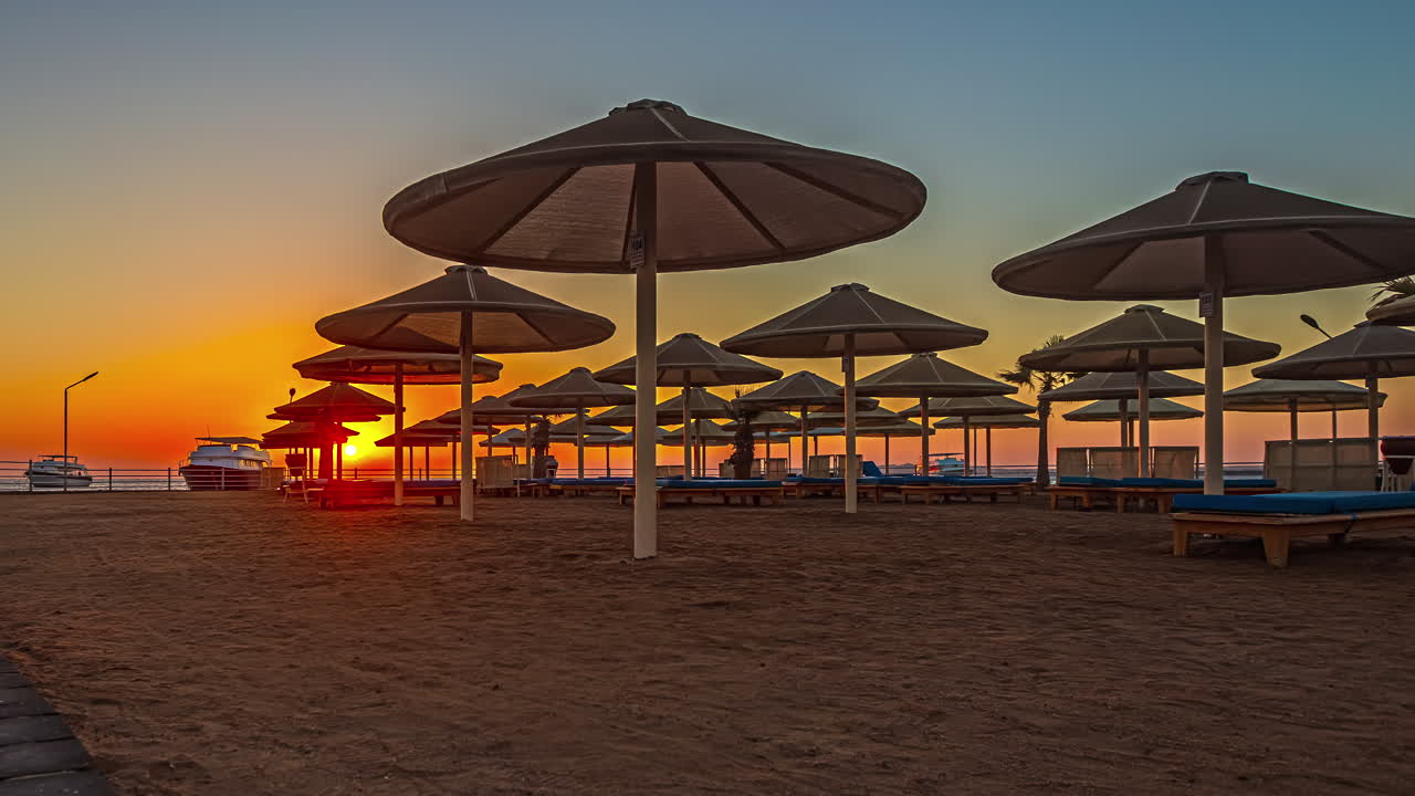 Lettini da hotel e ombrelloni tiki vuoti sulla spiaggia mentre il tramonto risplende nel cielo, Timelapse.