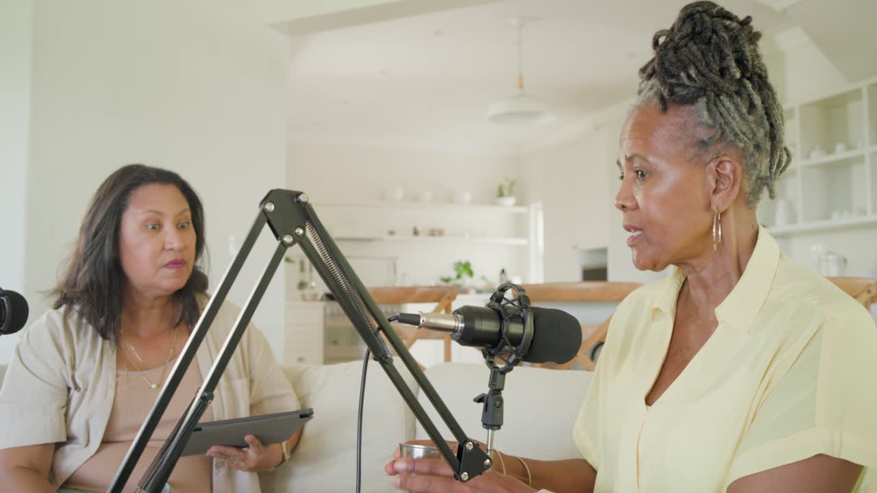 African American women co-hosts on couch recording right offering metal cup while speaking into mic