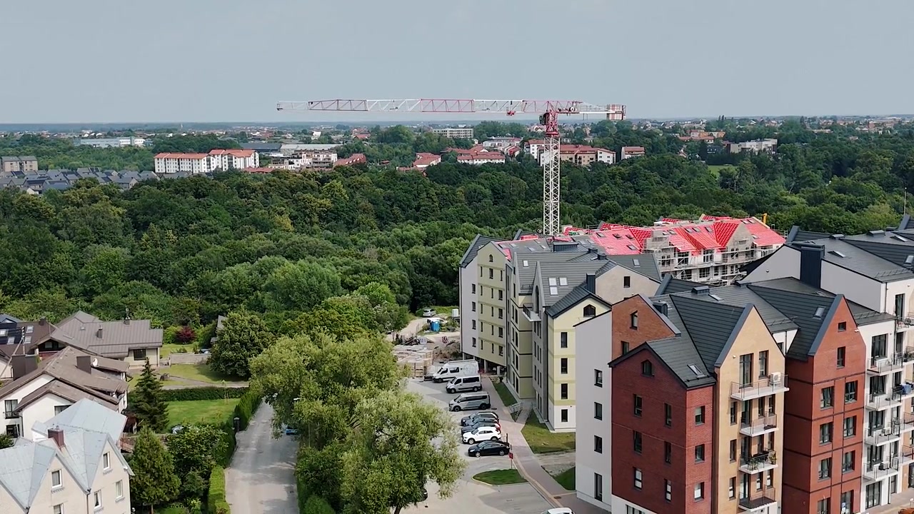 Moderne lejlighedsbygninger rejser sig ved siden af en stor grøn park, mens en tårnkran står over boligbyggepladsen.