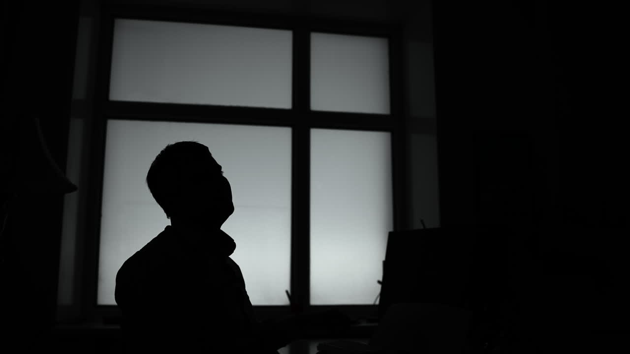 Uomo in silhouette che guarda in alto verso una finestra, direttore creativo in pausa per ispirazione, controluce soffuso. Media