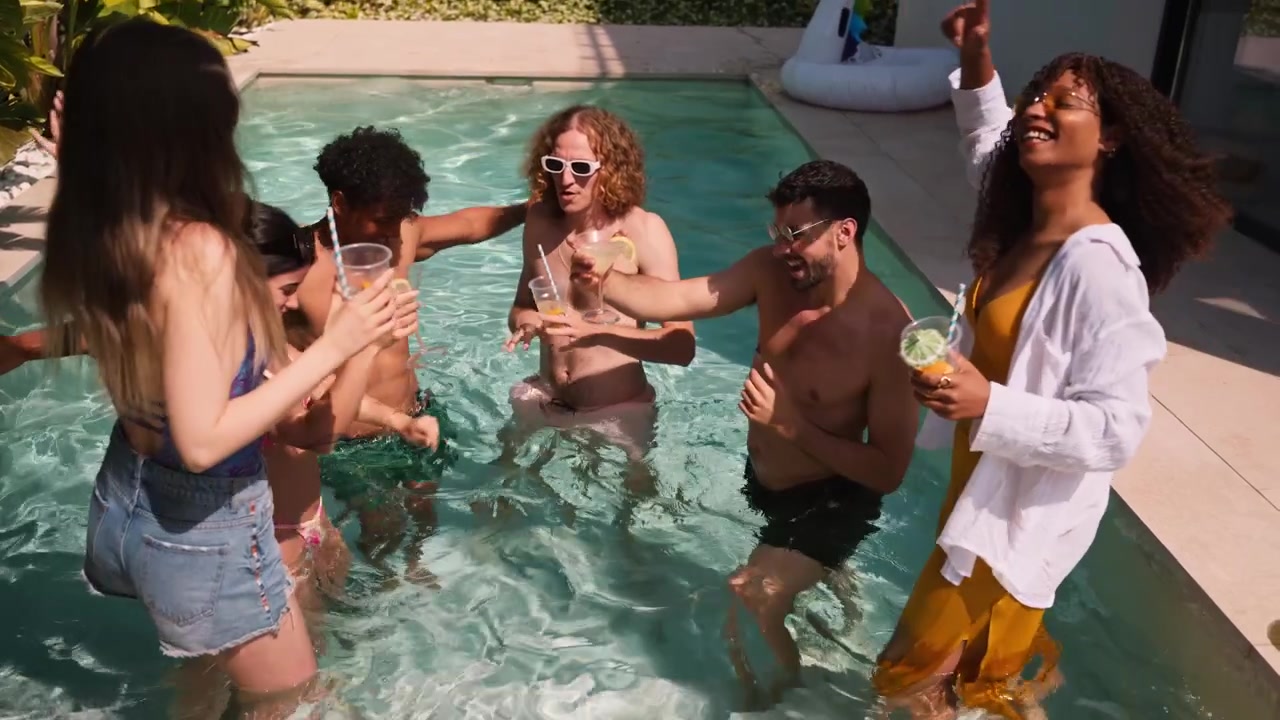 Amici felici di diverse etnie che brindano con cocktail in piscina