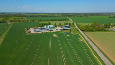 Drone-footage-flying-over-a-farm,-crops,-grain-elevators-and-several-farming-buildings