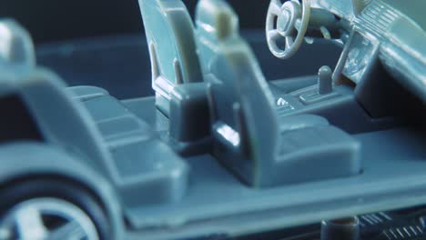 un diminuto modelo de esqueleto de muestra de metal de un coche en un soporte giratorio con luces de estudio, toma macro, vídeo de 4k, ruedas plateadas, neumáticos negros, puertas y ventanas, asientos de plástico gris
