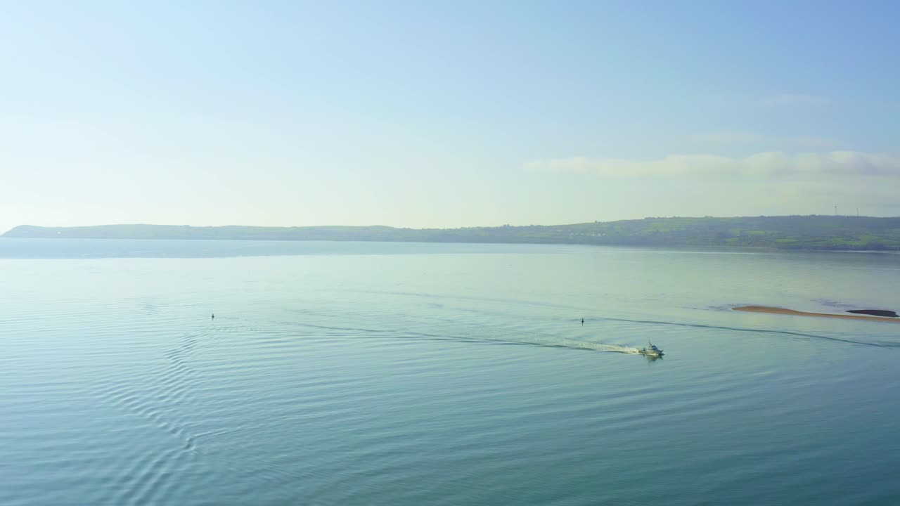 Aerial flying over blue ocean on sunny day, boat cruises by
