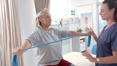 kaukasische physiotherapeutin hilft einer älteren patientin, mit widerstandsbändern zu trainieren