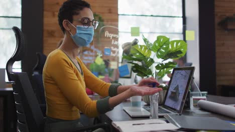 mujer caucásica con máscara facial usando desinfectante de manos en una oficina moderna