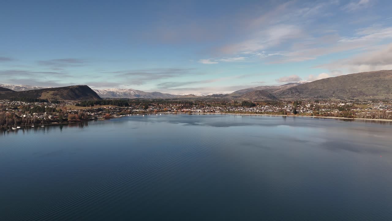 Acqua blu del lago e spiaggia costiera della città di Wanaka, Nuova Zelanda. Ampia ripresa aerea. Alba nella stagione autunnale. Cime innevate delle montagne in lontananza. Incantevole cittadina in Nuova Zelanda