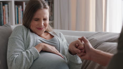 young pregnant woman going into labor having contractions nervous husband helping wife breath calmly through pregnancy pain relaxing on sofa at home
