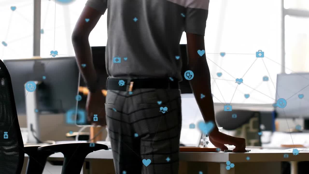 Animation of connected icons over african american man working on laptop at office