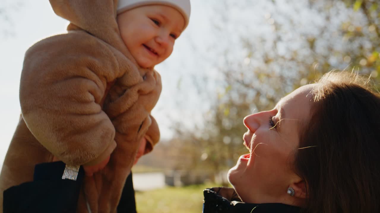 Eine fröhliche Mutter und ihr bezauberndes Kind umarmen sich in einer sonnendurchfluteten Outdoor-Szene und zeigen einen Moment der Liebe und des Glücks, während das Kind ein fröhliches Lächeln zeigt