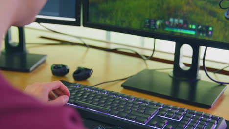 man making in game purchase using credit card and mobile phone at home sitting at desk with monitor