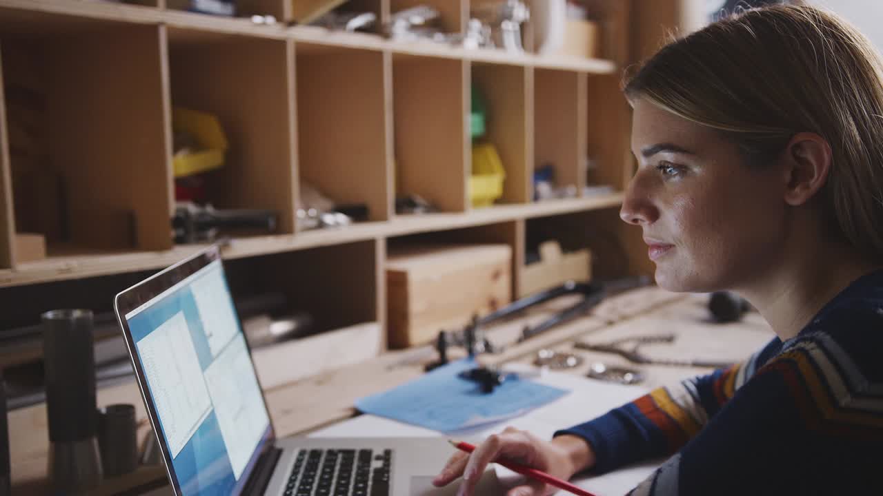 Close-up de engenheira em oficina usando laptop e fazendo anotações no plano para bicicleta