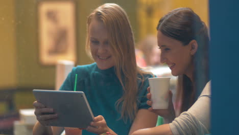 Mujeres-En-Un-Café-Riéndose-De-Algo-En-Una-Tableta