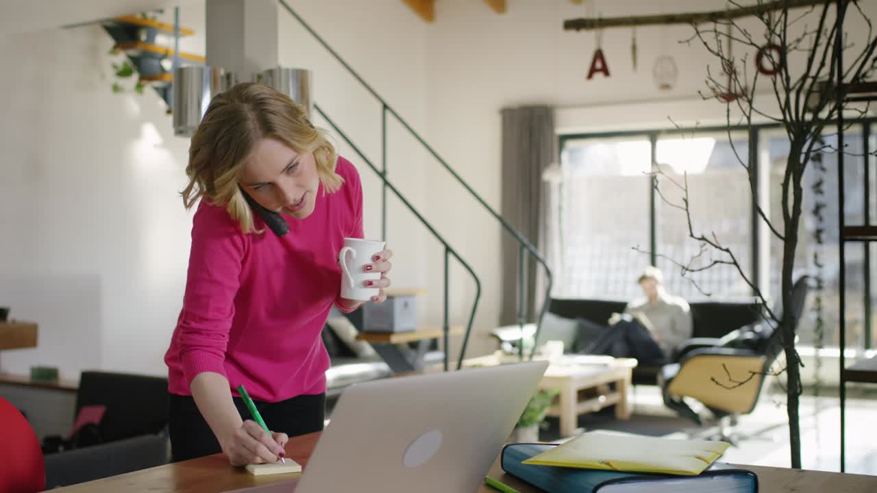 Cheerful Woman typing on Laptop while speaking on Handy at home