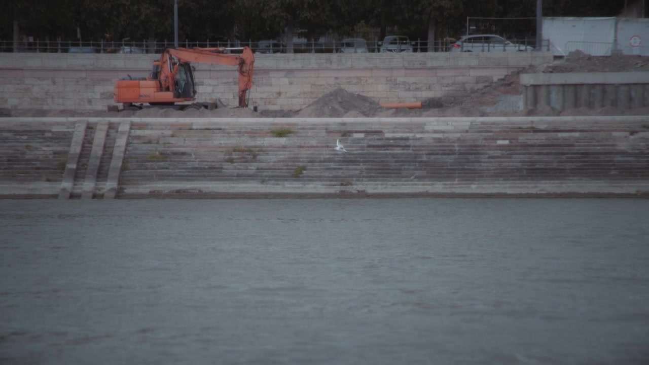 Gabbiano in volo sopra un fiume vicino a un cantiere con escavatore.