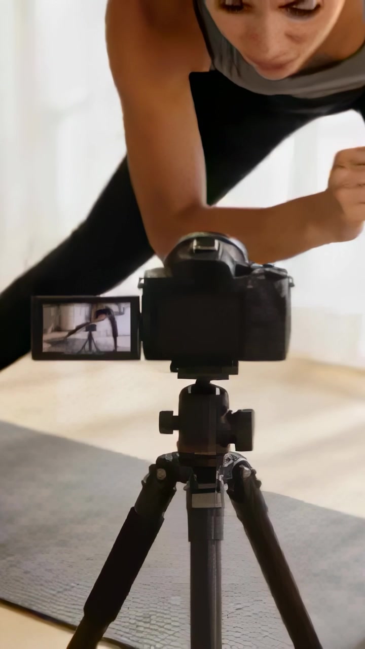 Video vertical: Profesional inclinándose revisando el encuadre, filmando a un lado haciendo zancadas en casa con equipo gris y pantalla abatible de DSLR